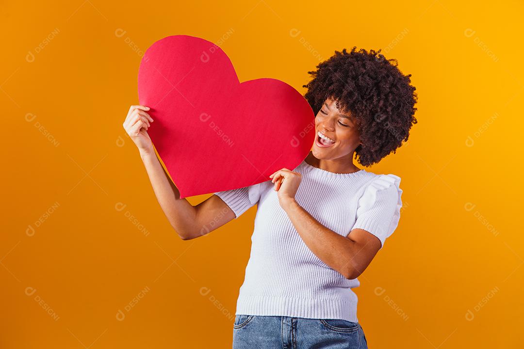 Mulher Afro sorridente segurando um grande cartão de coração vermelho