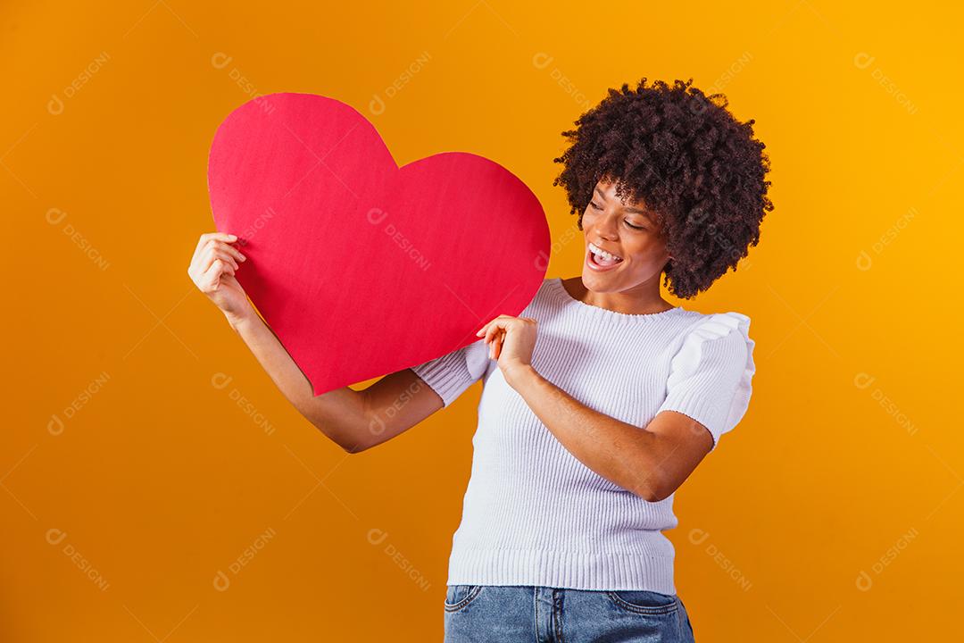 Mulher Afro sorridente segurando um grande cartão de coração vermelho