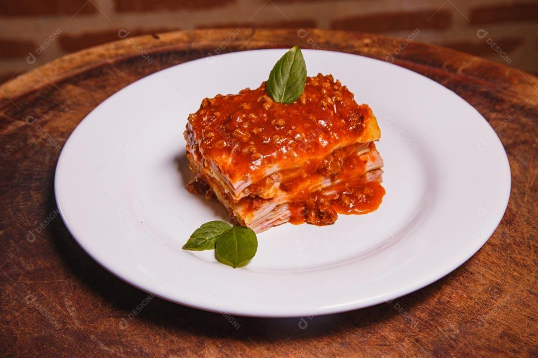 Prato de comida com lasanha e temperos verdes sobre mesa de madeira