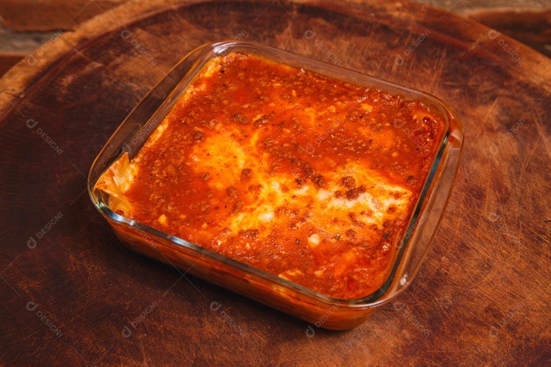 Forma de vidro com lasanha e temperos verdes sobre mesa de madeira