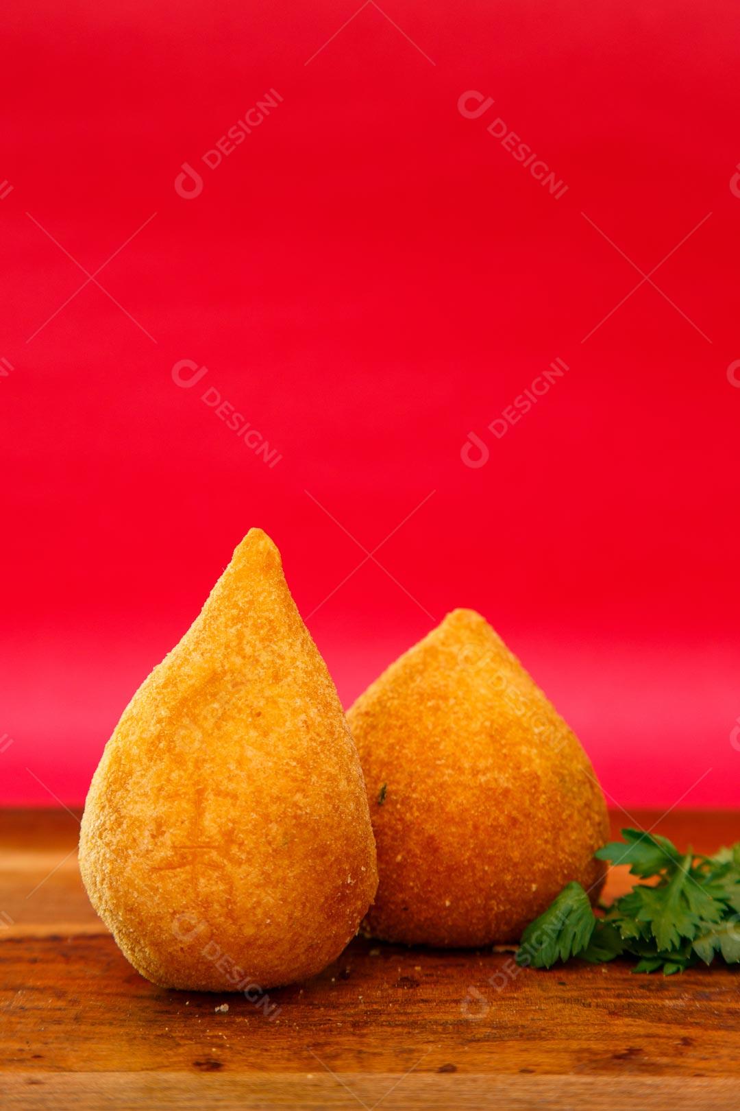 Coxinhas sobre mesa com temperos verdes fundo vermelho