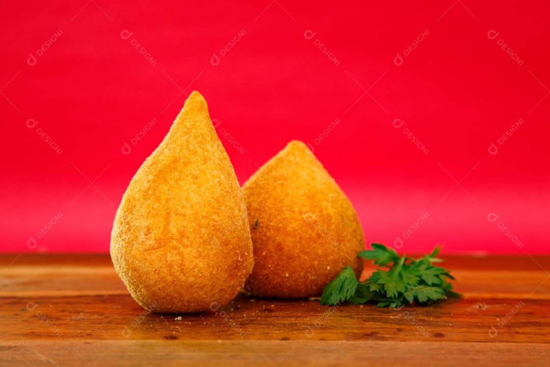 Coxinhas sobre mesa com temperos verdes fundo vermelho