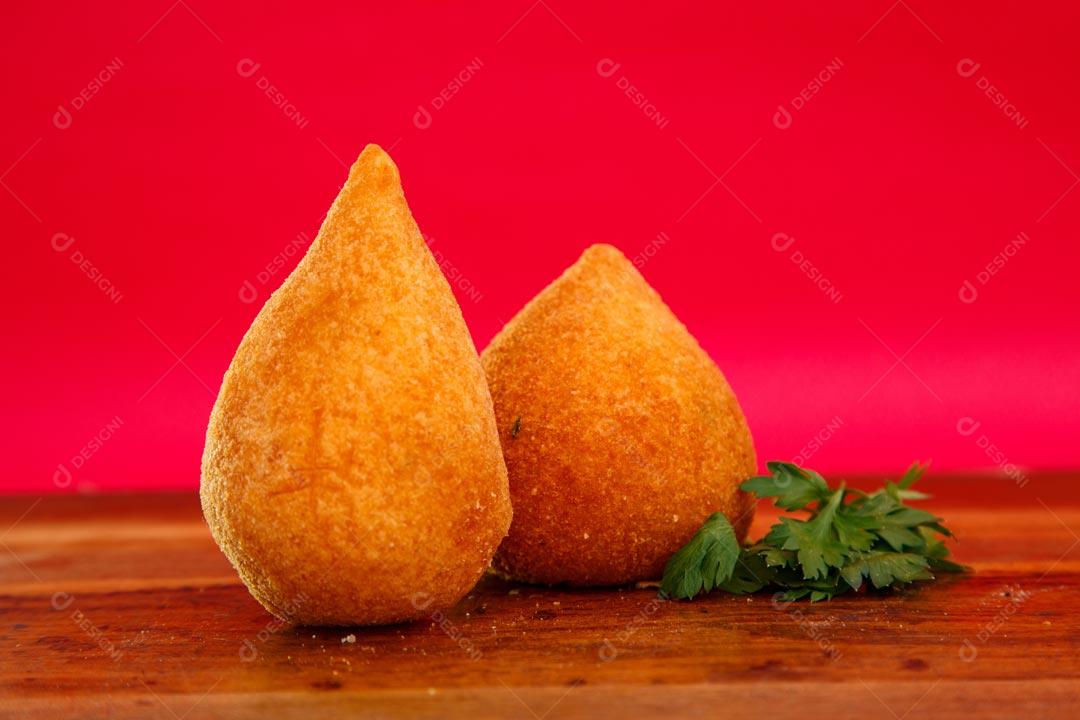 Coxinhas sobre mesa com temperos verdes fundo vermelho