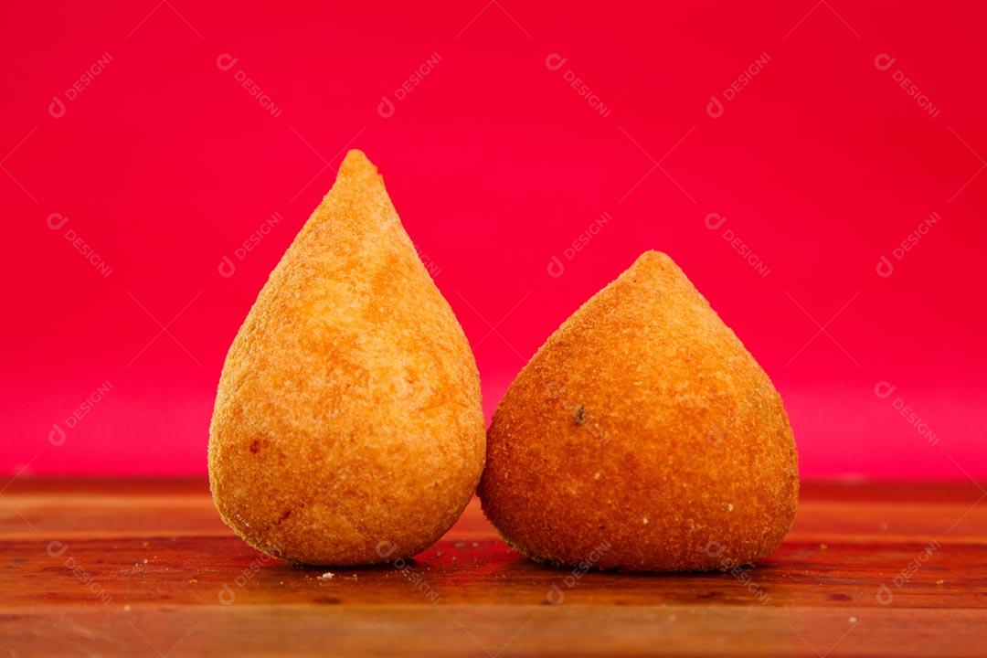 Coxinhas sobre mesa com temperos verdes fundo vermelho