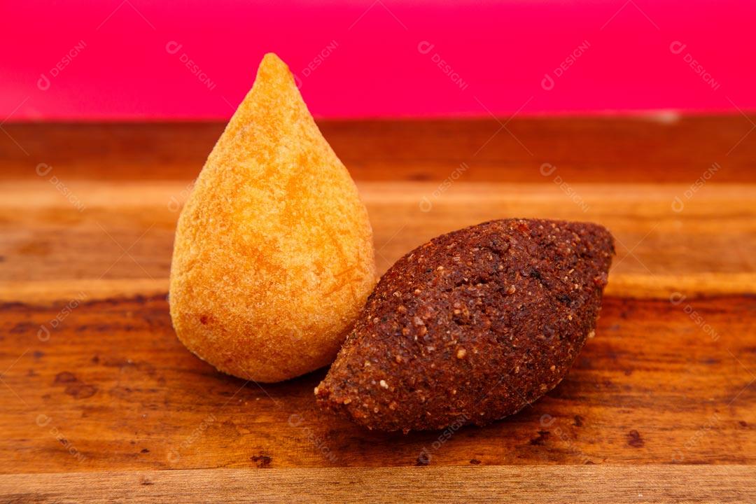 Coxinhas e Kibes sobre mesa com temperos verdes fundo vermelho