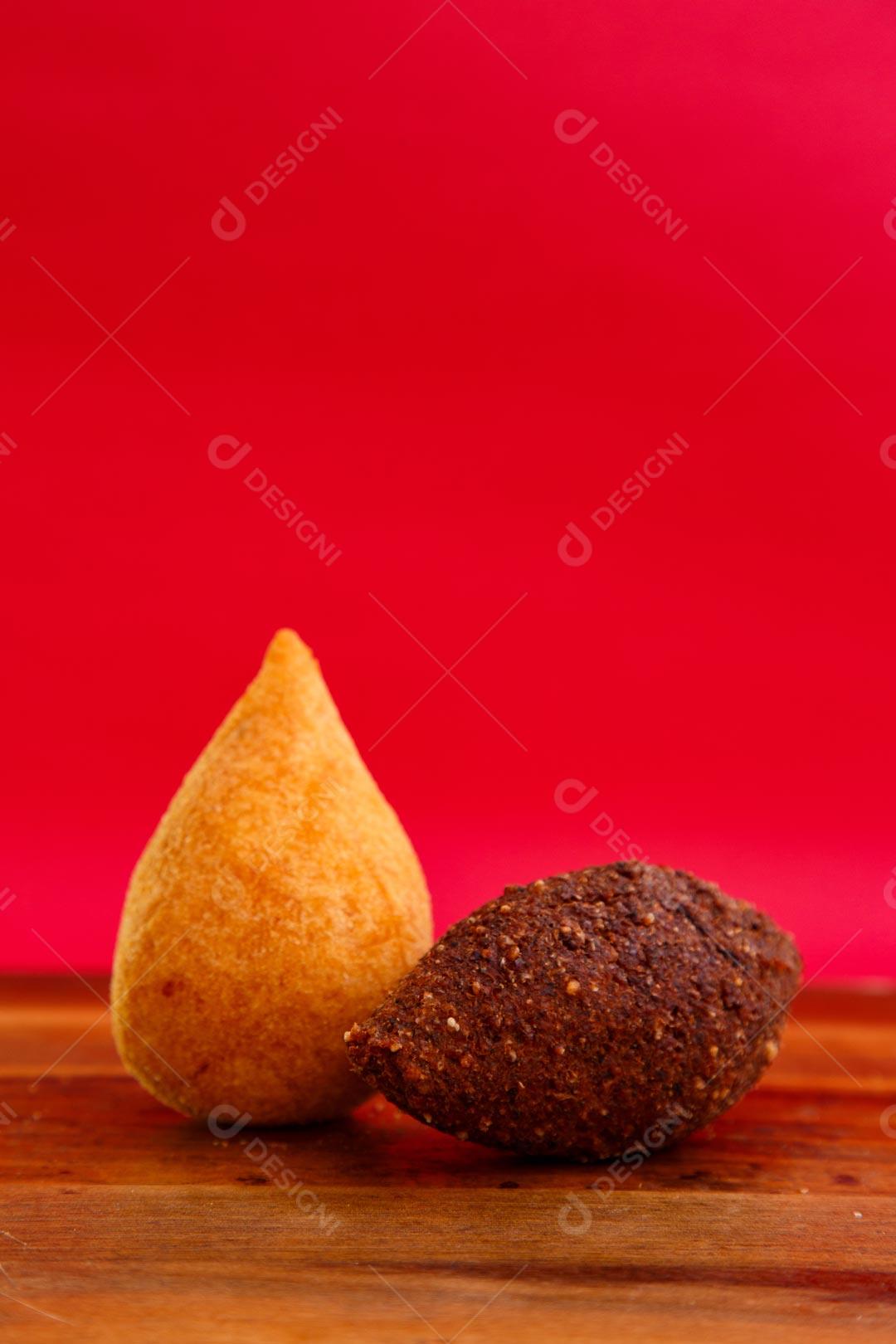 Coxinhas e Kibes sobre mesa com temperos verdes fundo vermelho