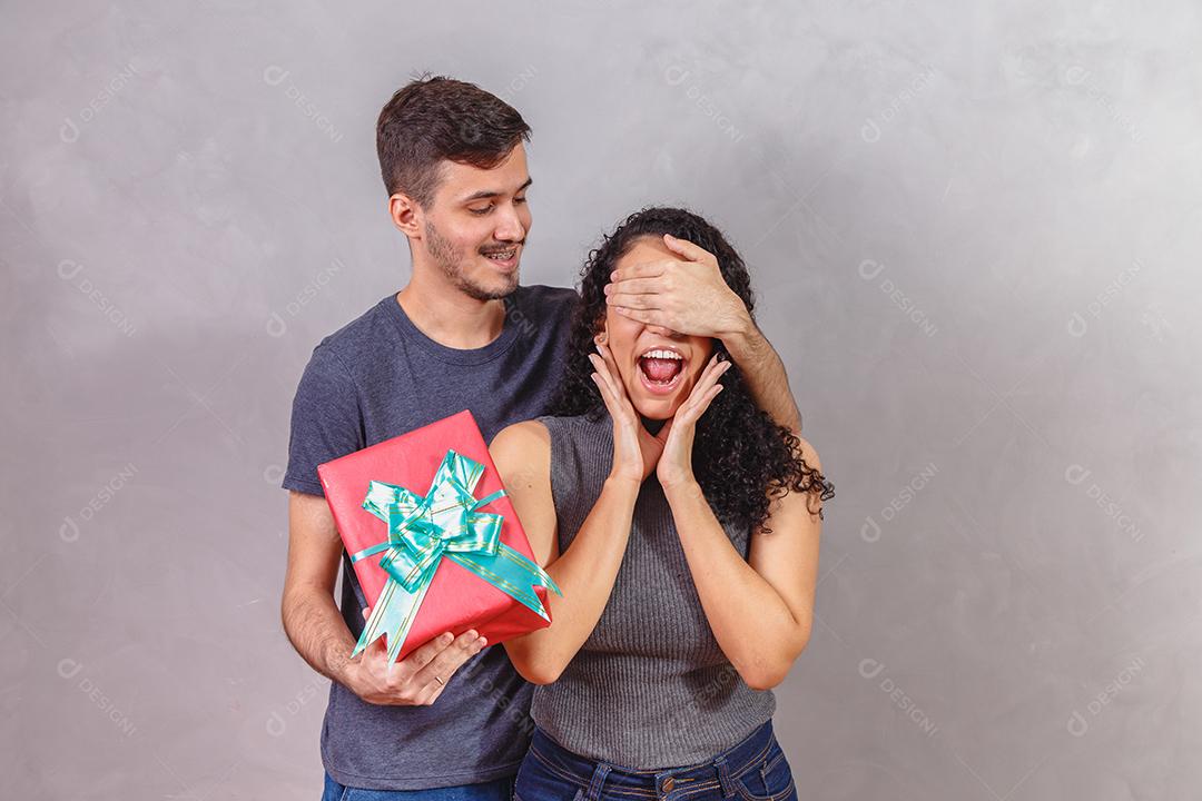 Jovem bonito está cobrindo os olhos da namorada e dando um Presente