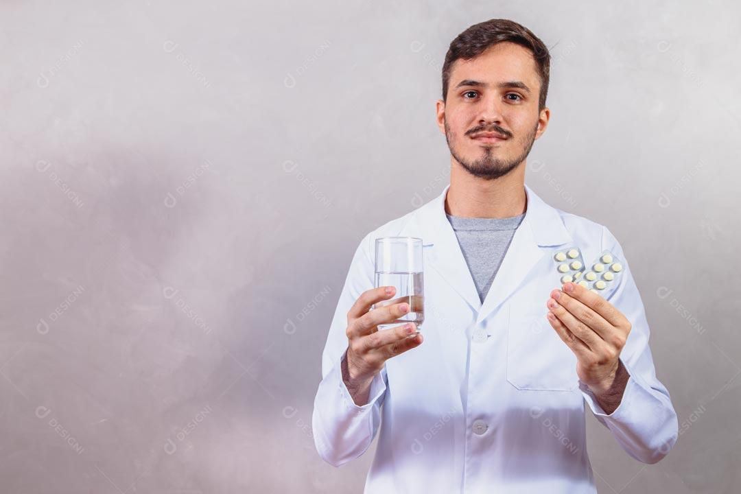 Homem Médico Com Jaleco Branco Segurando Copo de Água e Comprimidos