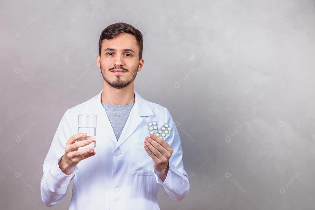 Homem Médico Com Jaleco Branco Segurando Copo de Água e Comprimidos