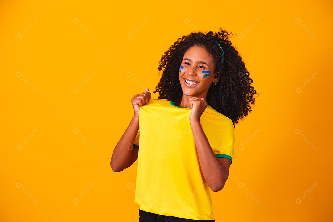 Mulher de cabelo cacheado e camiseta amarela do brasil em fundo amarelo