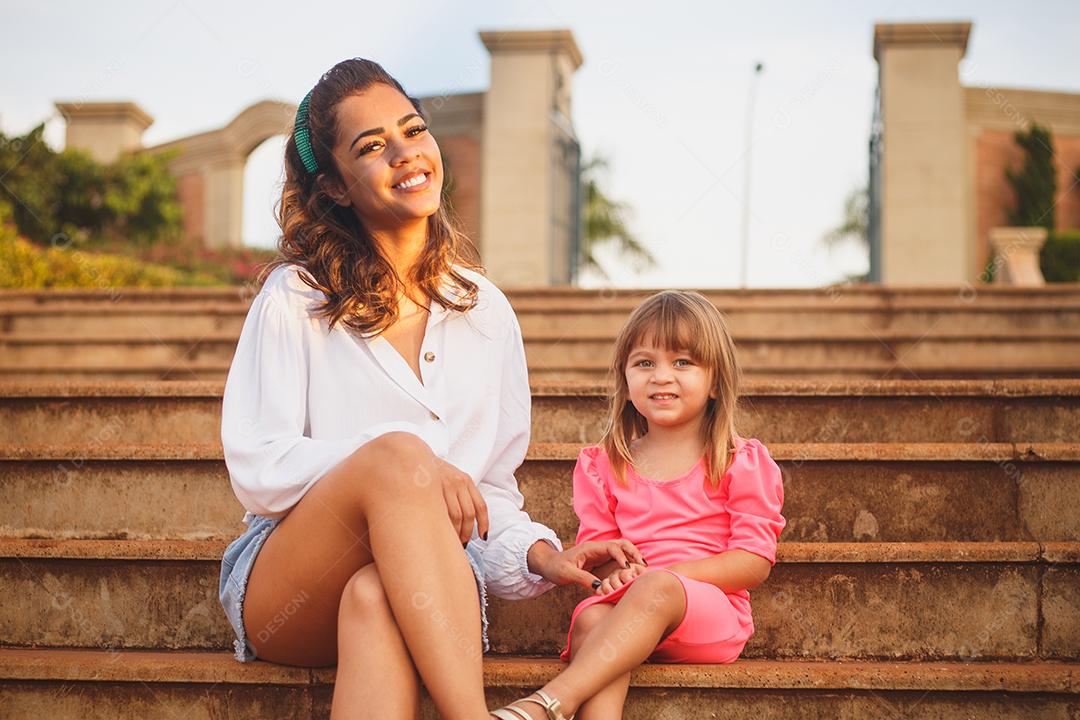 Mãe e filha juntas em praça florida em fim de dia