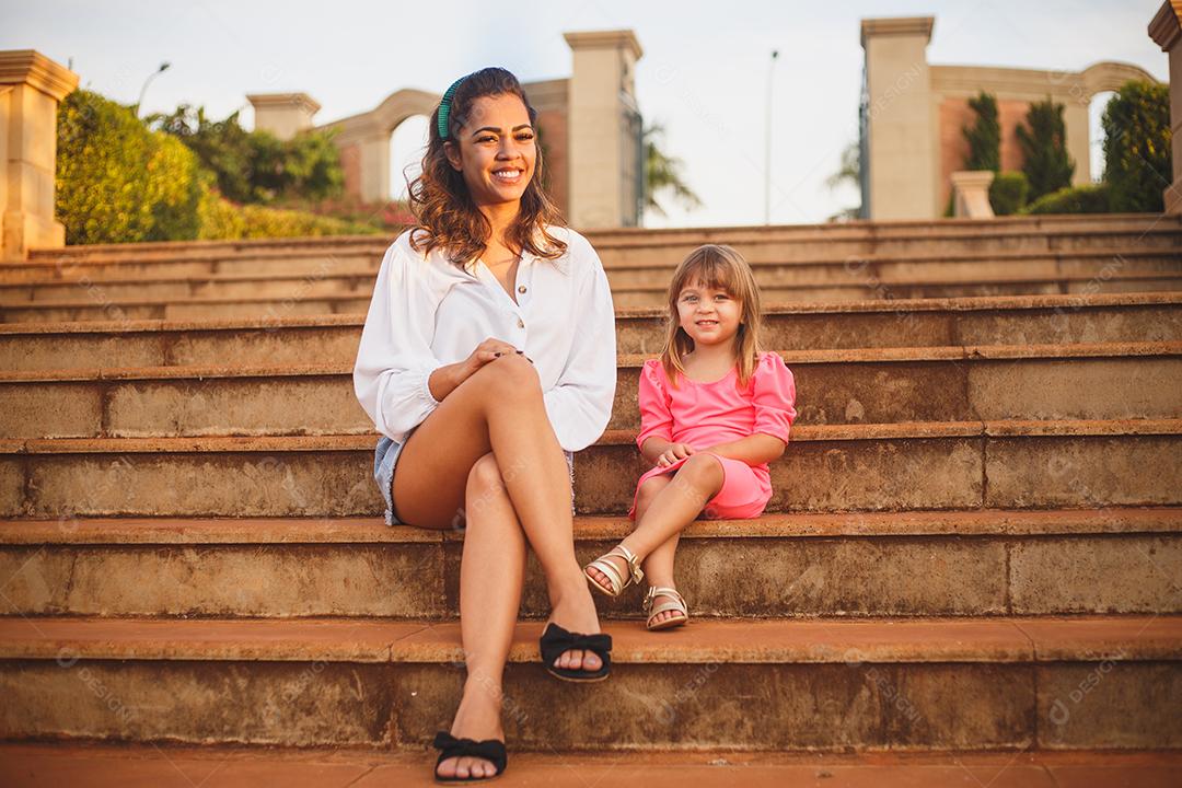 Mãe e filha juntas em praça florida em fim de dia