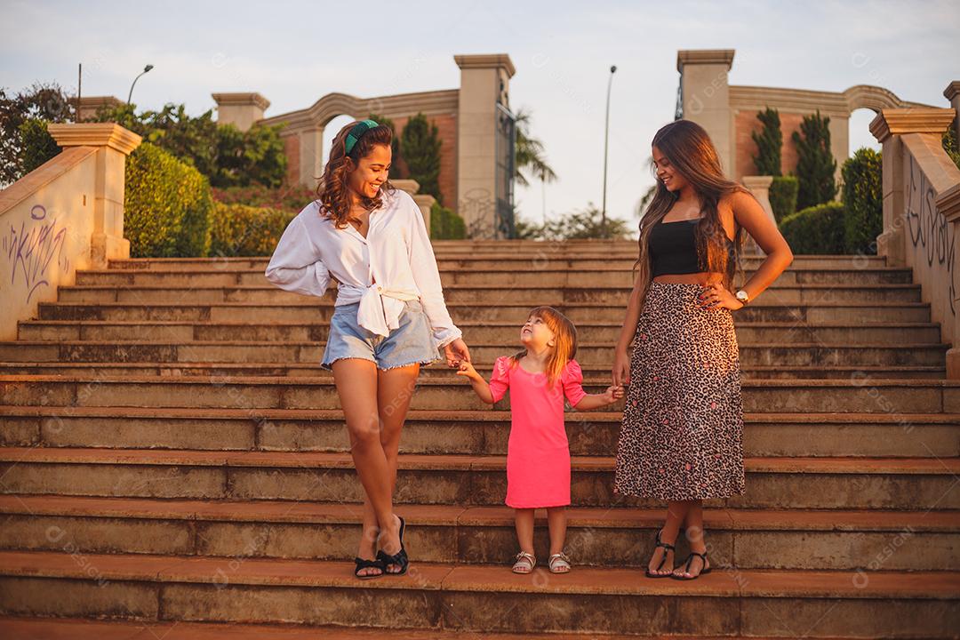 Mãe e filhas juntas em praça florida em fim de dia