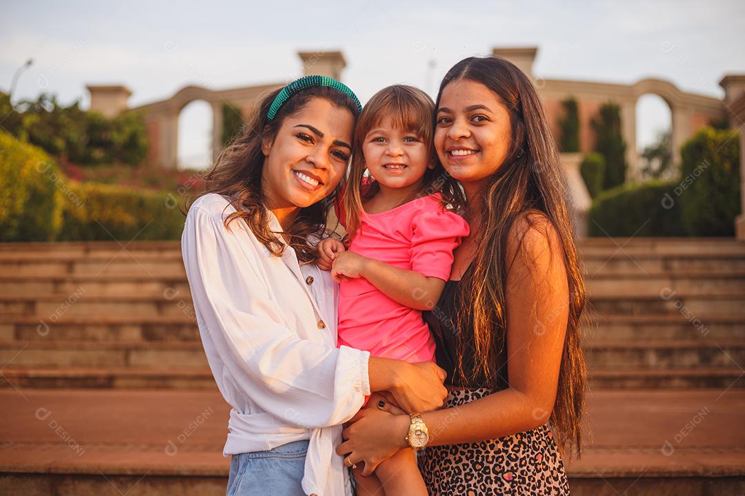Mãe e filhas juntas em praça florida em fim de dia