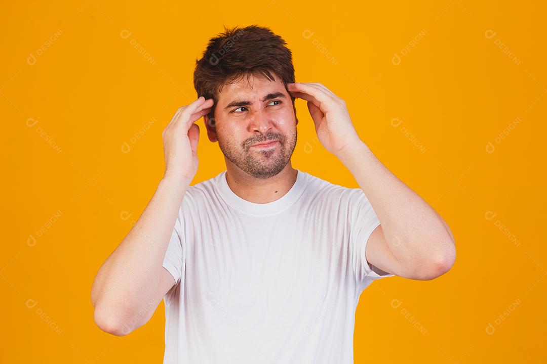 Jovem bonito vestindo uma camiseta branca com a mão na cabeça para dor de cabeça por causa do estresse. Sofrendo de enxaqueca.