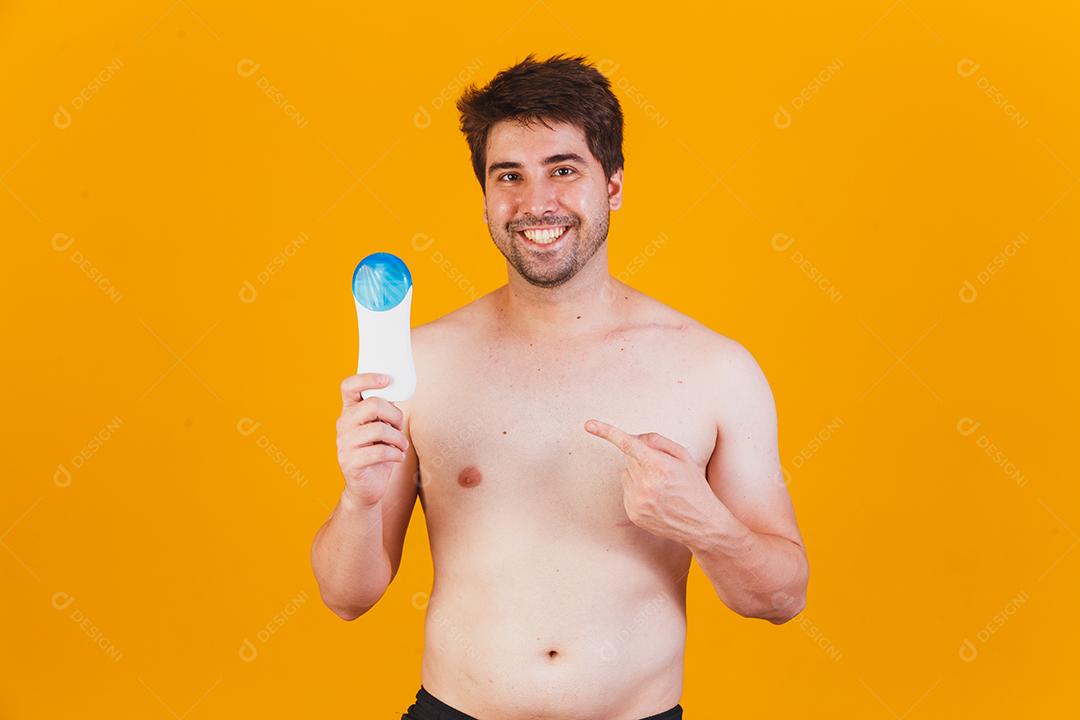 Homem bonito com barba de férias vestindo trajes de banho segurando o frasco de protetor solar olhando positivo