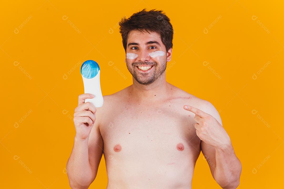 Homem bonito com barba de férias vestindo trajes de banho segurando o frasco de protetor solar olhando positivo
