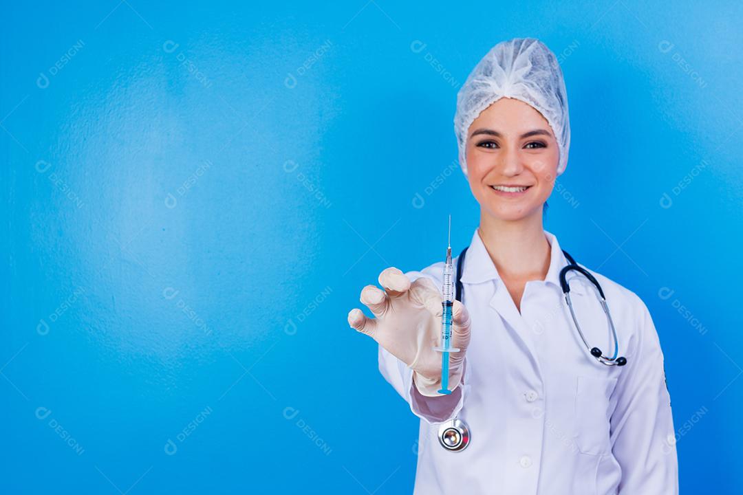 Mulher médica com jaleco e estetoscópio segurando agulha em fundo azul