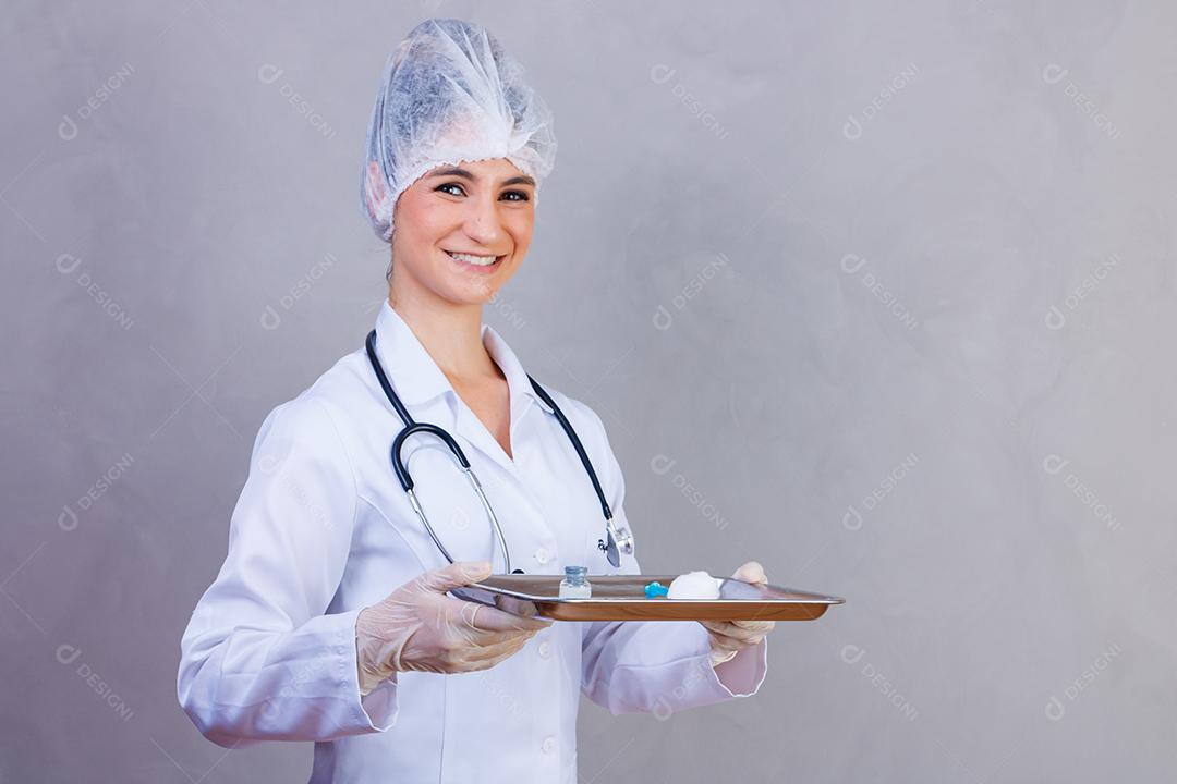 Mulher médica segurando bandeja com jaleco e estetoscópio em fundo azul