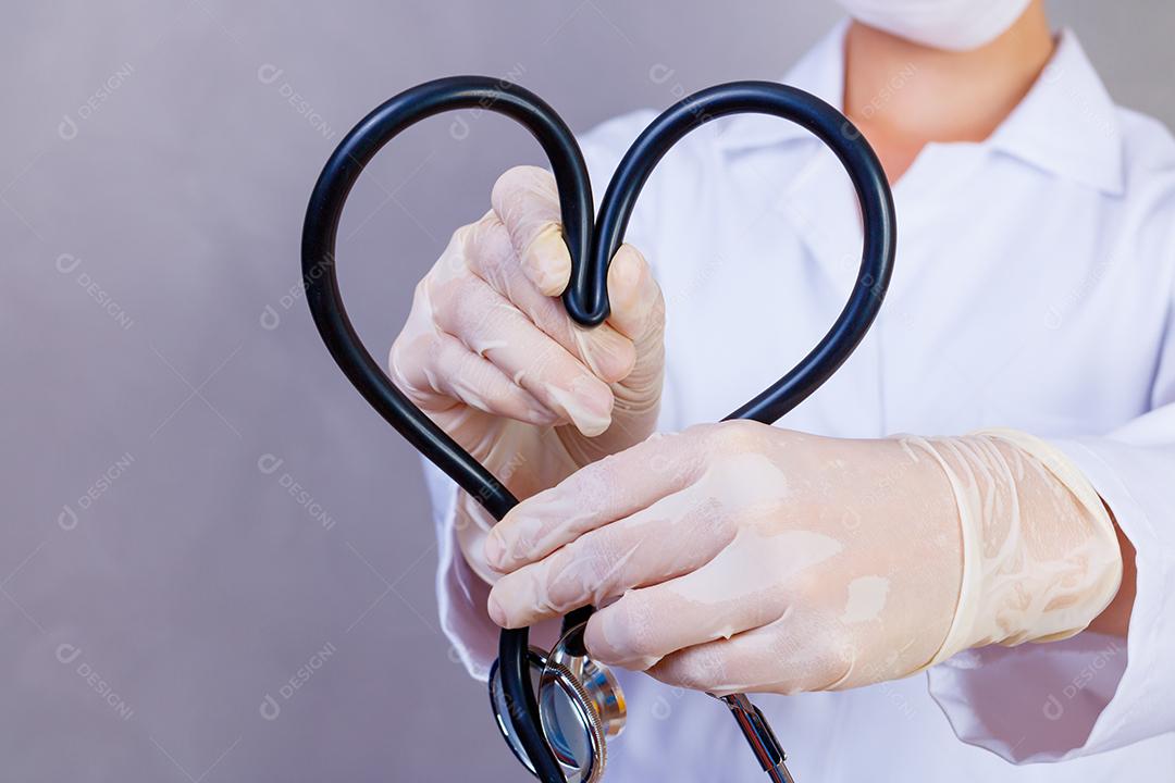 Mulher médica com jaleco e estetoscópio em forma de coração em fundo cinza