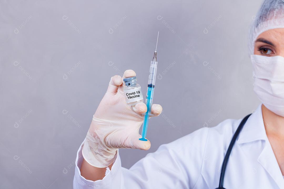 Mulher médica com jaleco e estetoscópio segurando vacina em fundo cinza