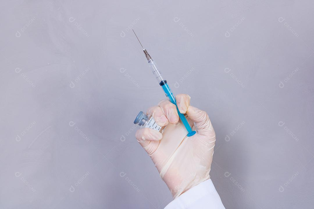 Mulher médica com jaleco e estetoscópio segurando vacina em fundo cinza