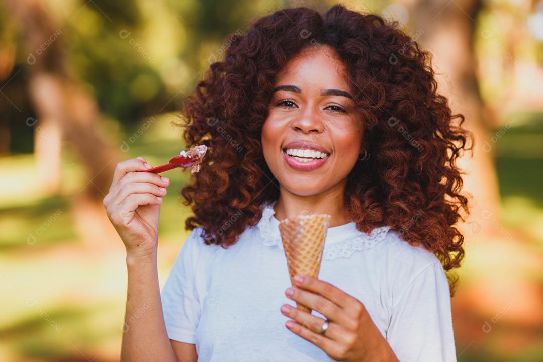 Mulher afro feliz tomando sorvete no parque.