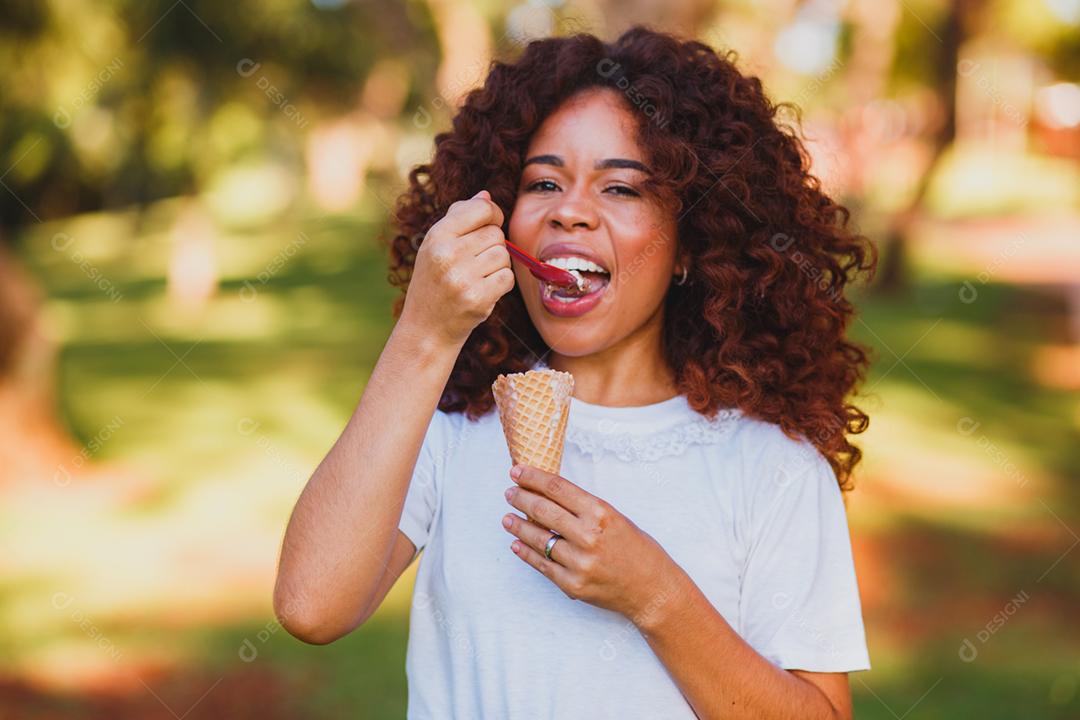 Mulher afro feliz tomando sorvete no parque.