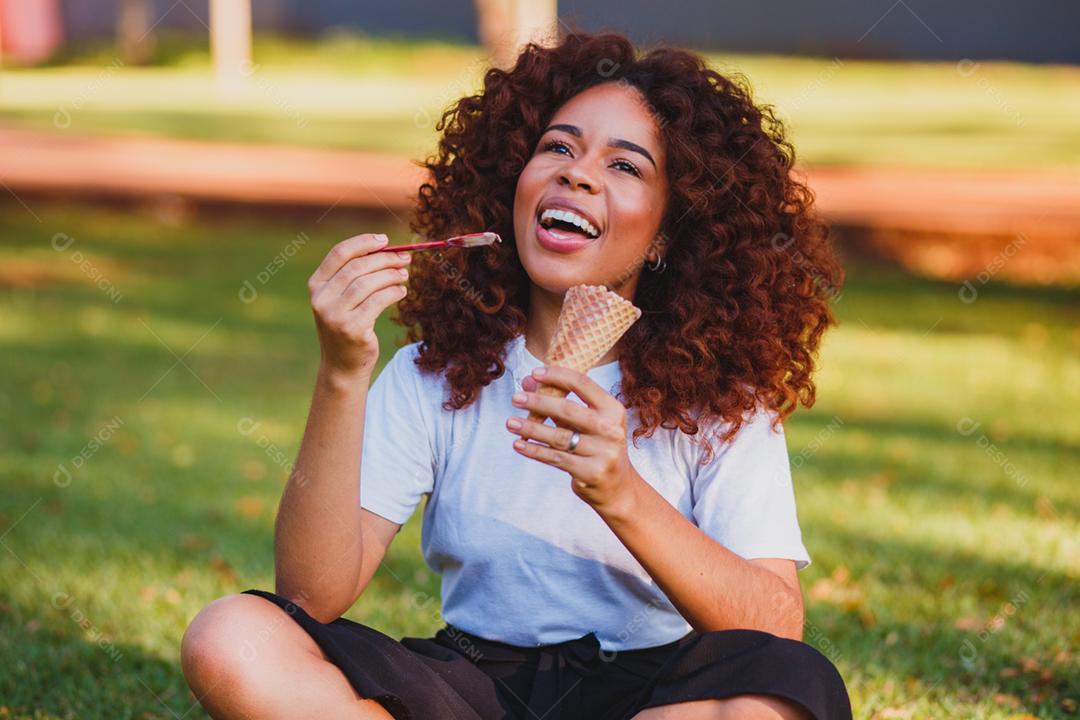 Mulher afro feliz tomando sorvete no parque.