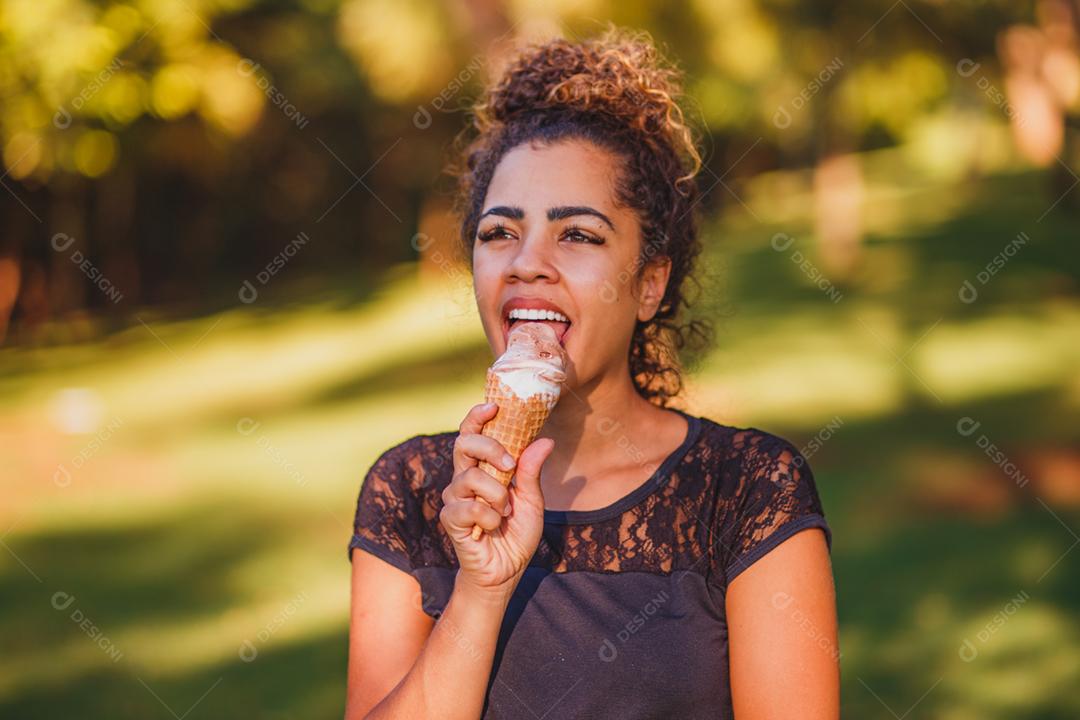 Mulher afro feliz tomando sorvete no parque.