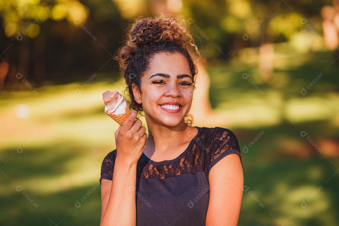 Mulher afro feliz tomando sorvete no parque.