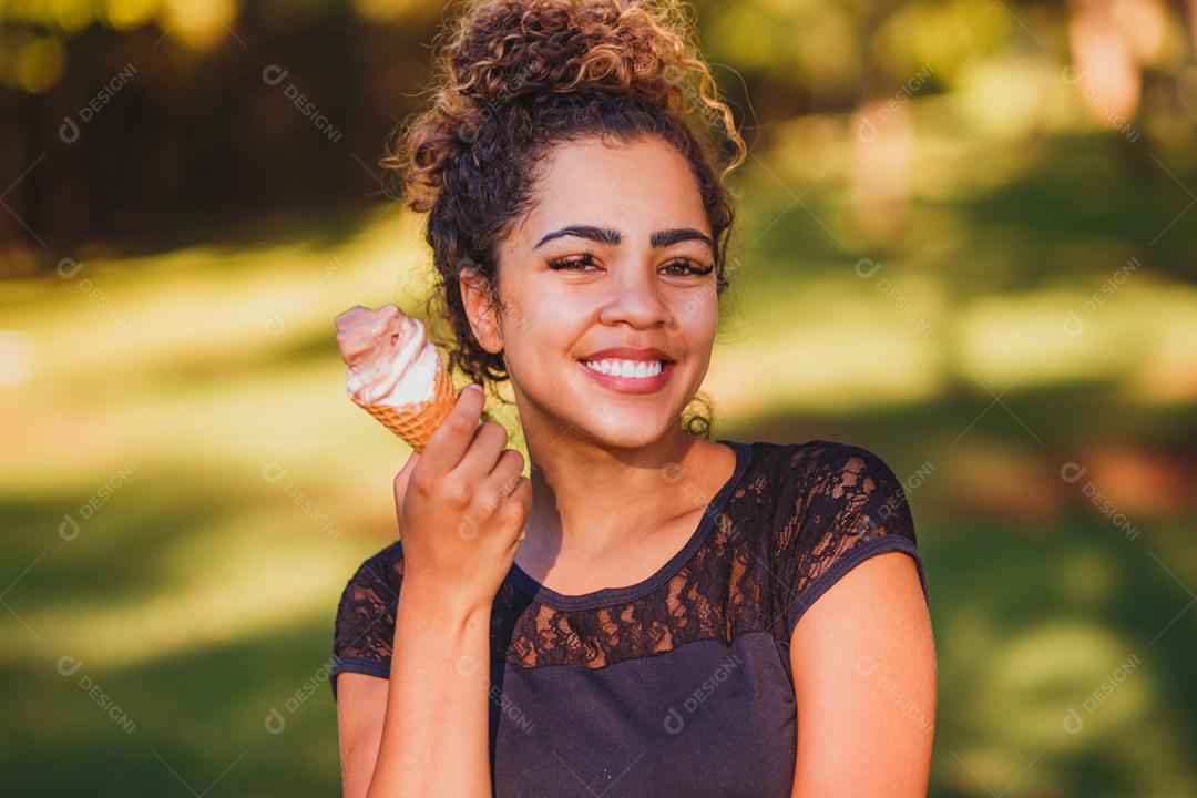 Mulher afro feliz tomando sorvete no parque.