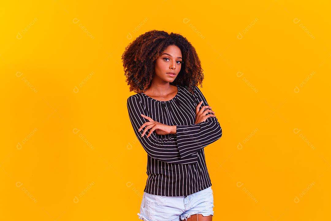 Mulher afro cruza os braços em fundo amarelo