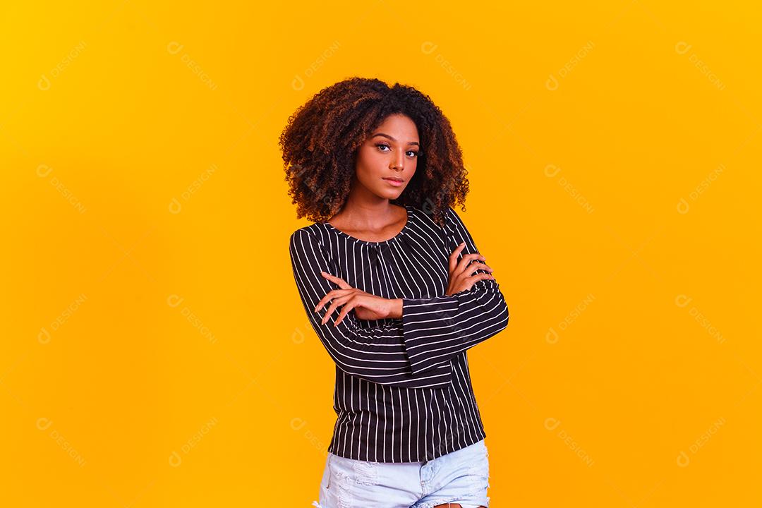 Mulher afro cruza os braços em fundo amarelo