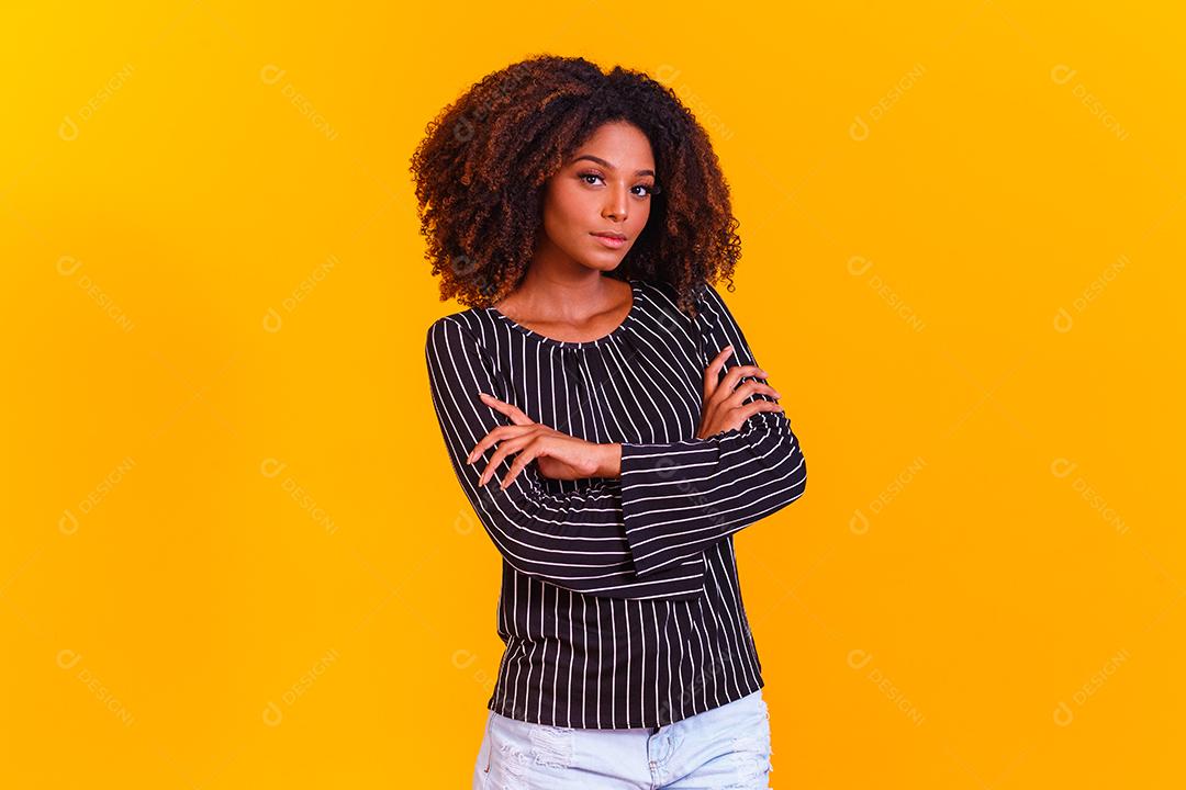 Mulher afro cruza os braços em fundo amarelo