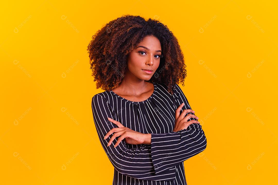 Mulher afro com braços os cruzados em fundo amarelo