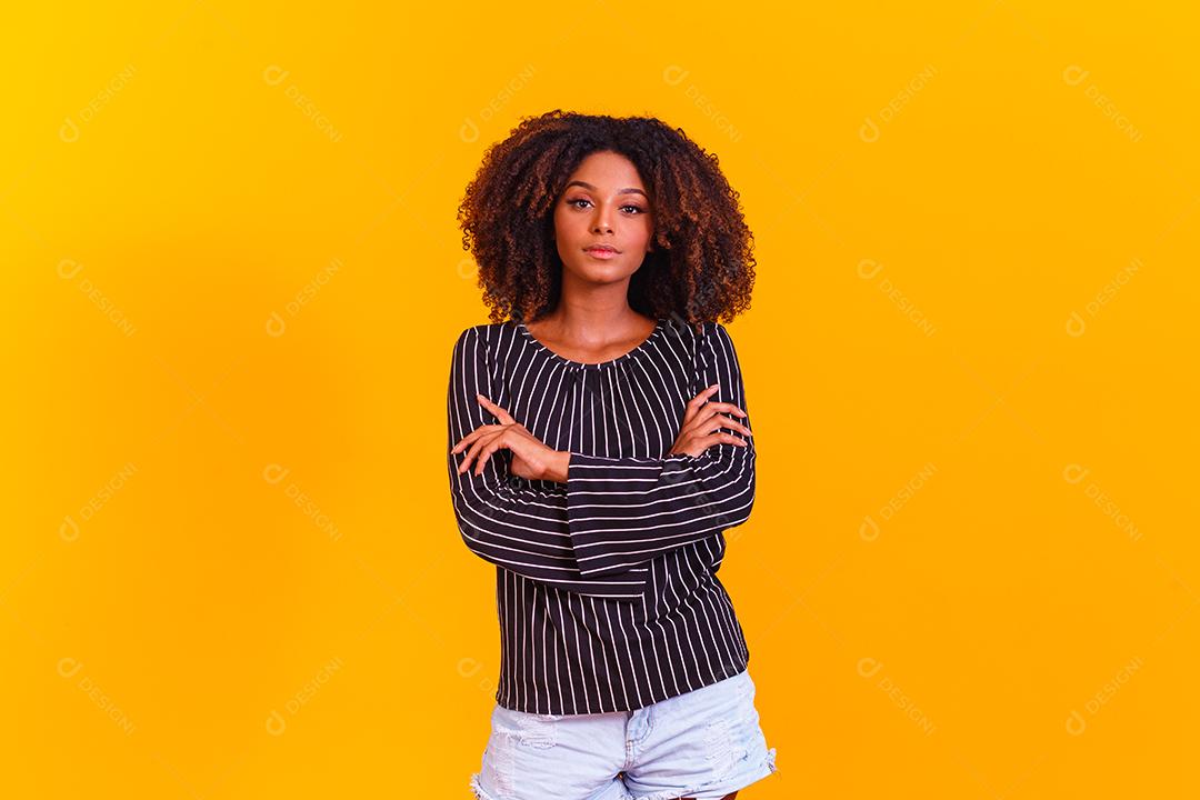 Mulher afro cruza os braços em fundo amarelo