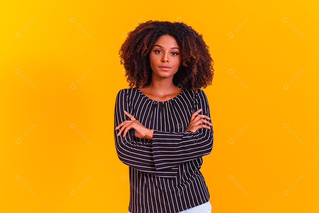 Mulher afro cruza os braços em fundo amarelo
