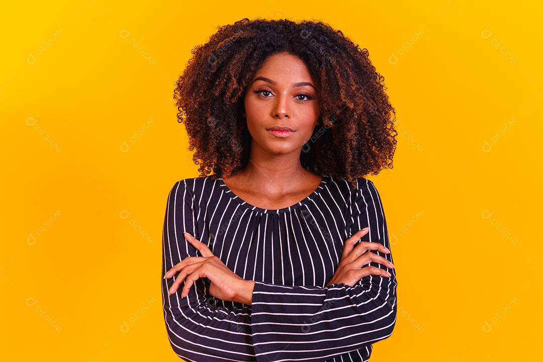 Mulher afro cruza os braços em fundo amarelo