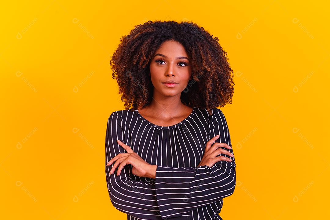 Mulher afro cruza os braços em fundo amarelo