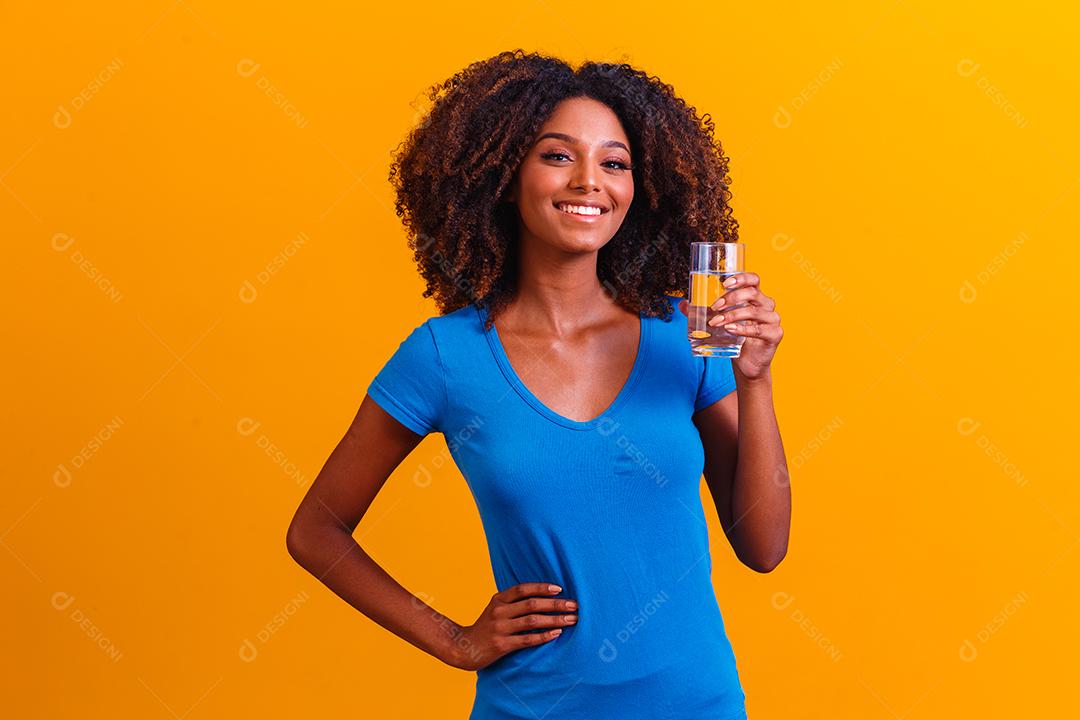 jovem negra bebendo água em fundo amarelo. Moça com copo de água