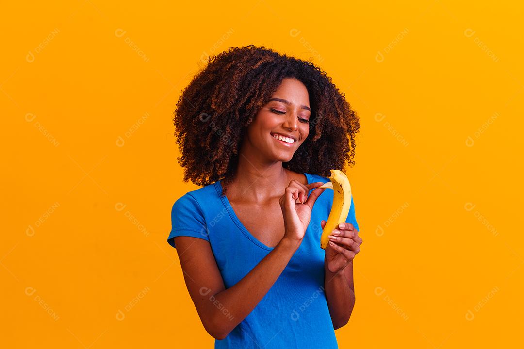 Smiling brunette woman holding banana on yellow background