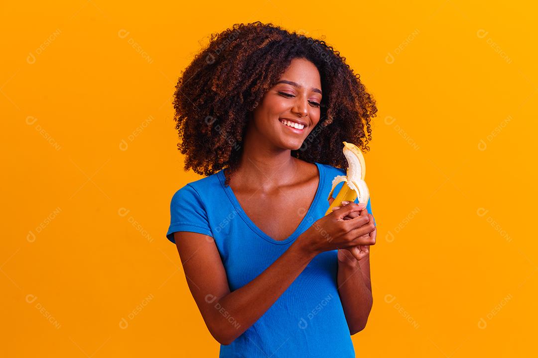 Mulher morena sorrindo segurando banana em fundo amarelo