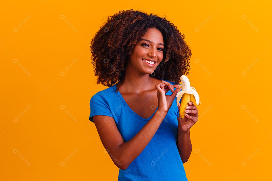 Mulher morena sorrindo segurando banana em fundo amarelo