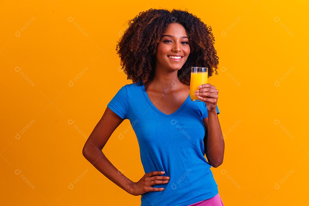 Mulher afro-americana bebendo suco de laranja em fundo amarelo