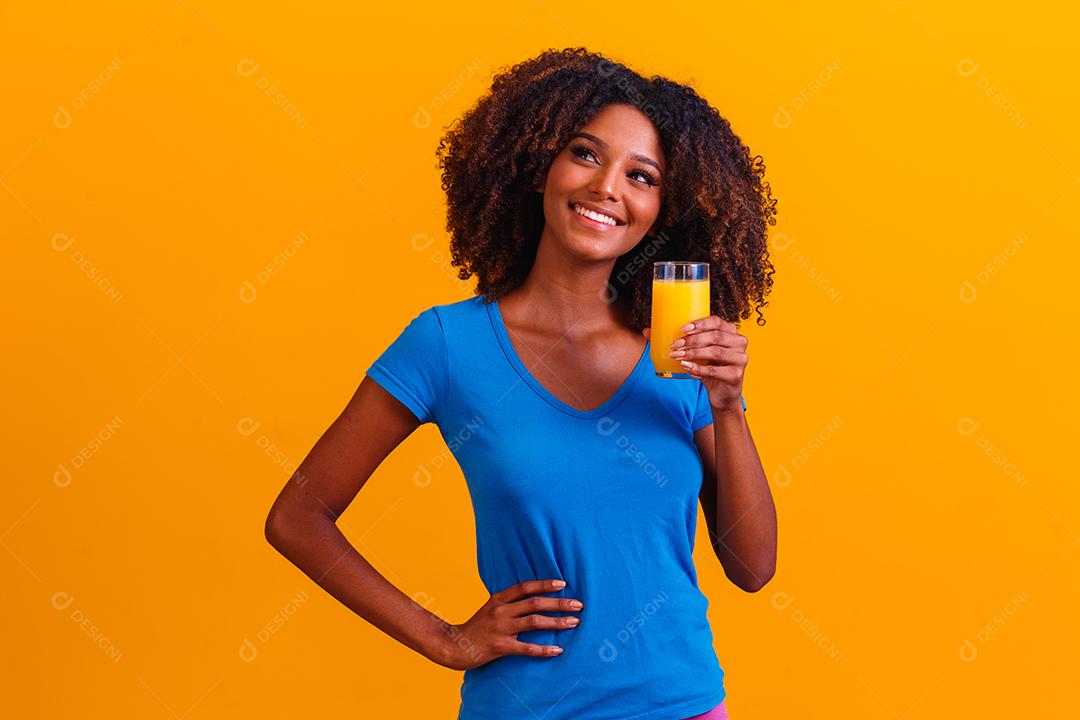 Mulher afro-americana bebendo suco de laranja em fundo amarelo