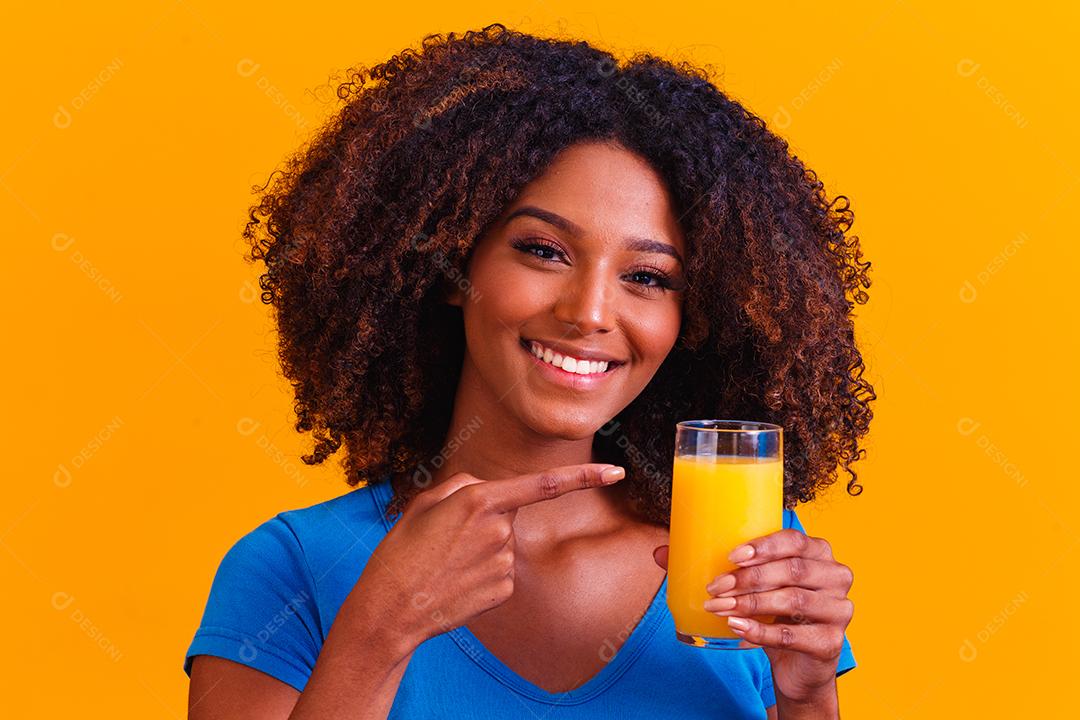 Mulher afro-americana bebendo suco de laranja em fundo amarelo