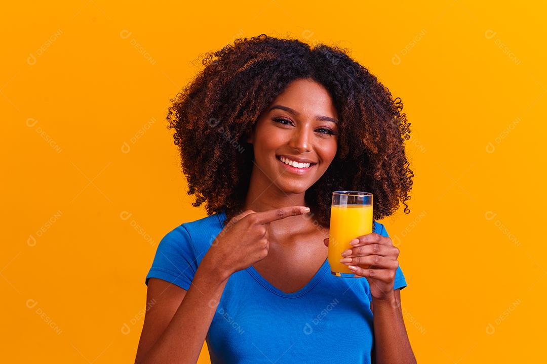 Mulher afro-americana bebendo suco de laranja em fundo amarelo