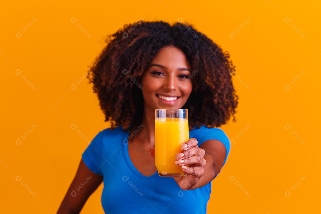 Mulher afro-americana bebendo suco de laranja em fundo amarelo