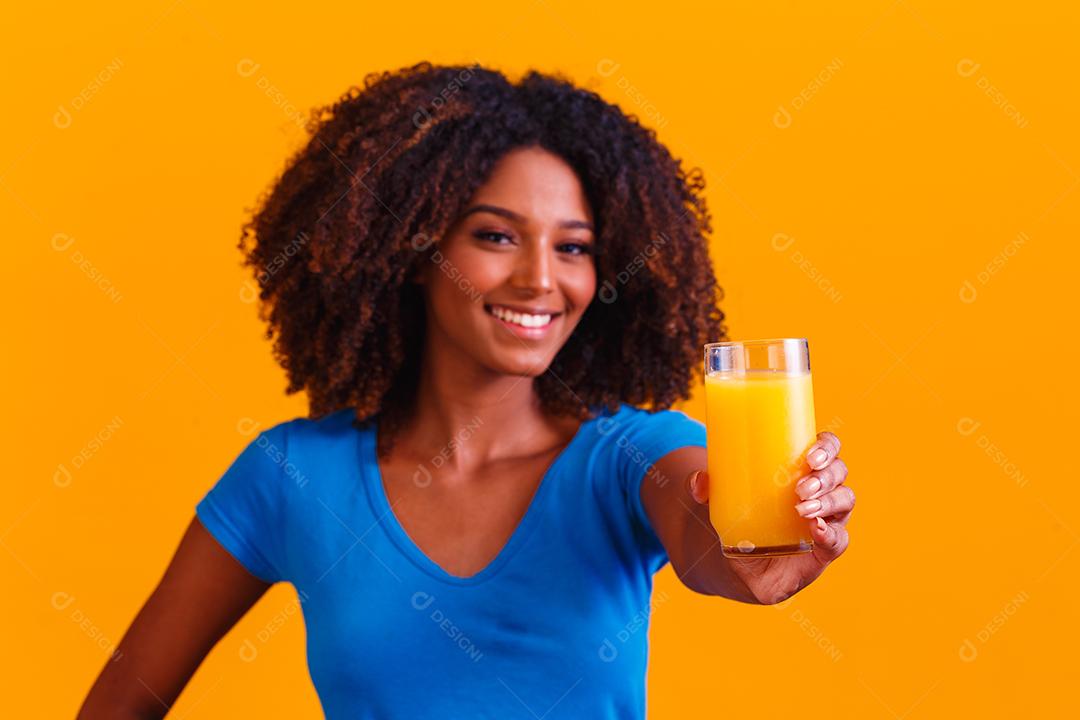 Mulher afro-americana bebendo suco de laranja em fundo amarelo